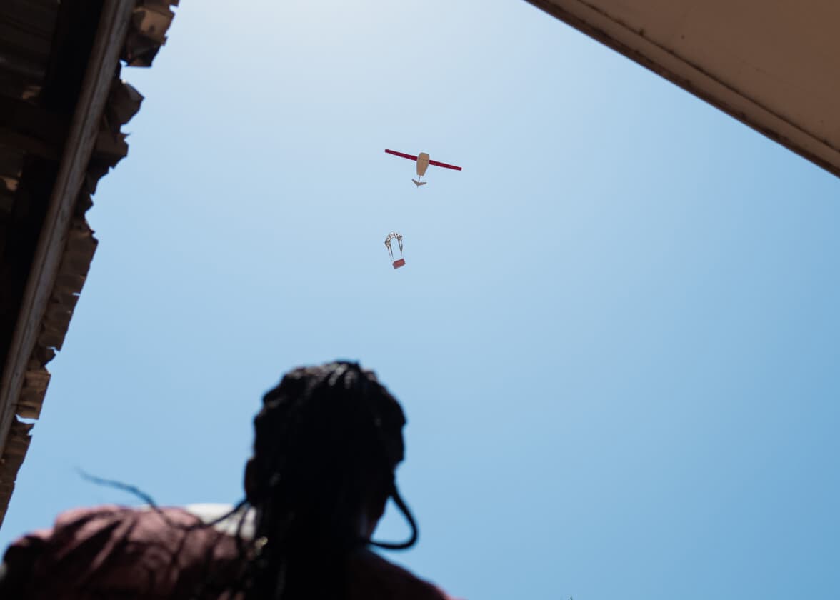Person watching a Zipline drone dropping a parachute package overhead.